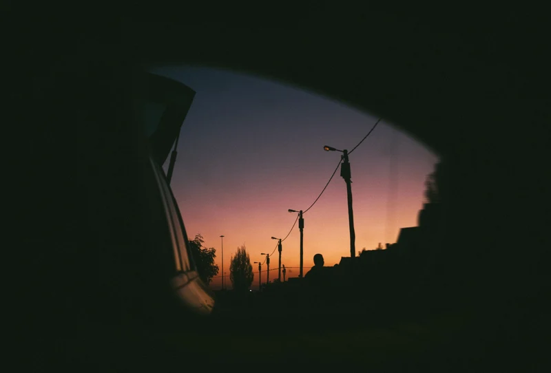 Street lights against a sunset sky, framed by a car window