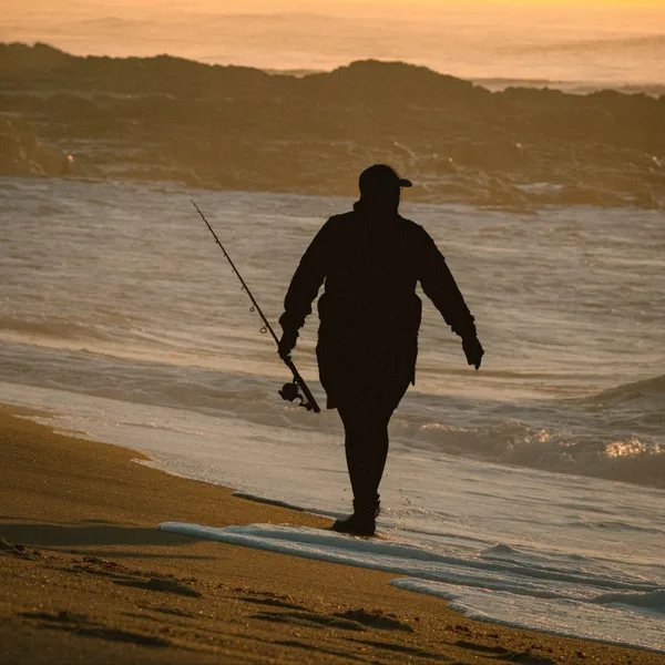 Silhouette of a fisherman carrying his rod along the shoreline at sunset