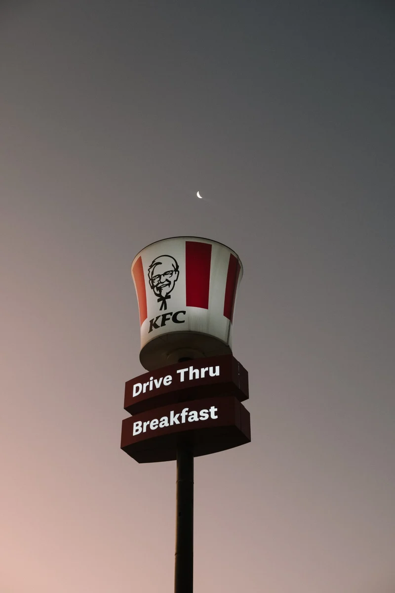 Lit KFC bucket sign under a crescent moon at dusk