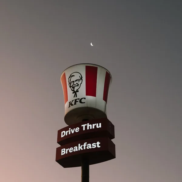 Lit KFC bucket sign under a crescent moon at dusk
