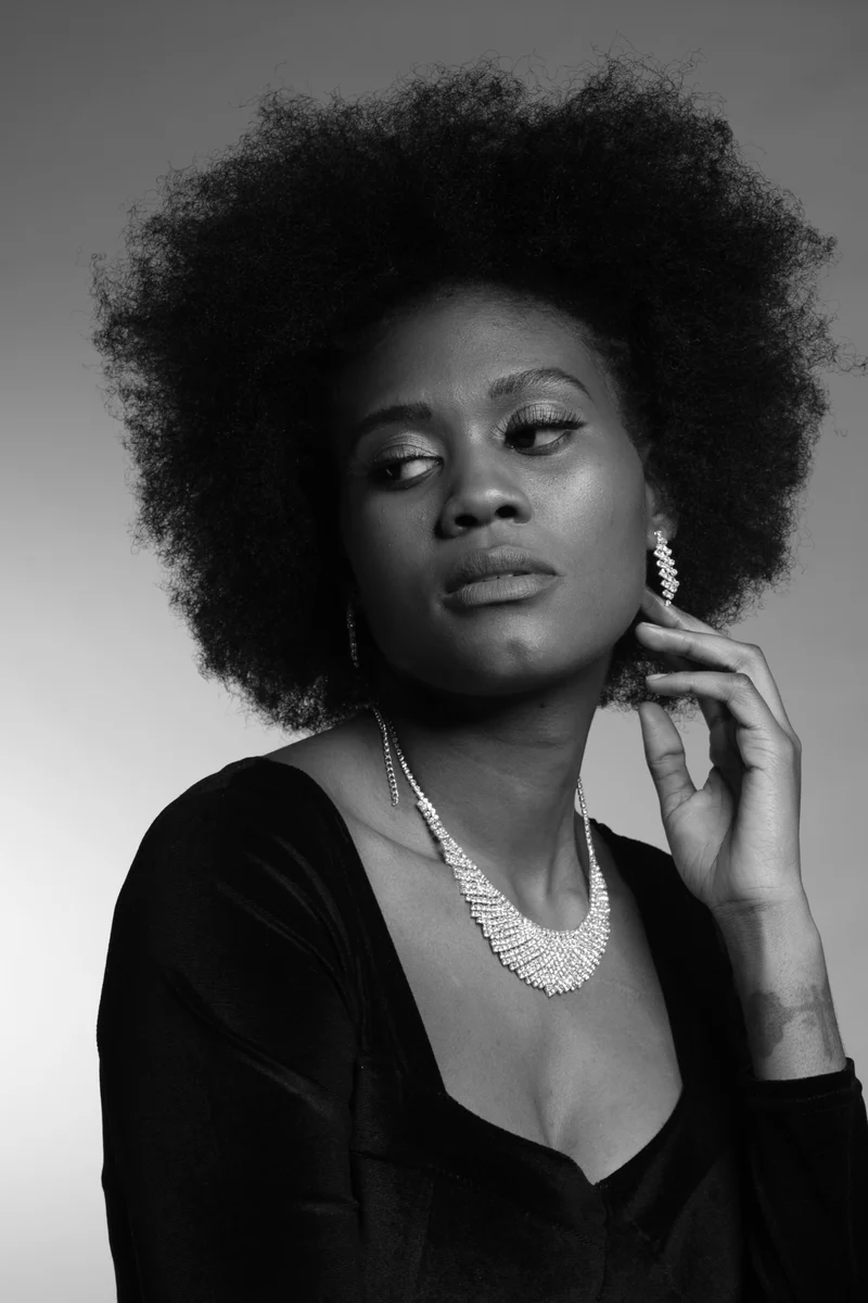 Black-and-white studio portrait of a woman with an afro and a crystal necklace, looking over her shoulder