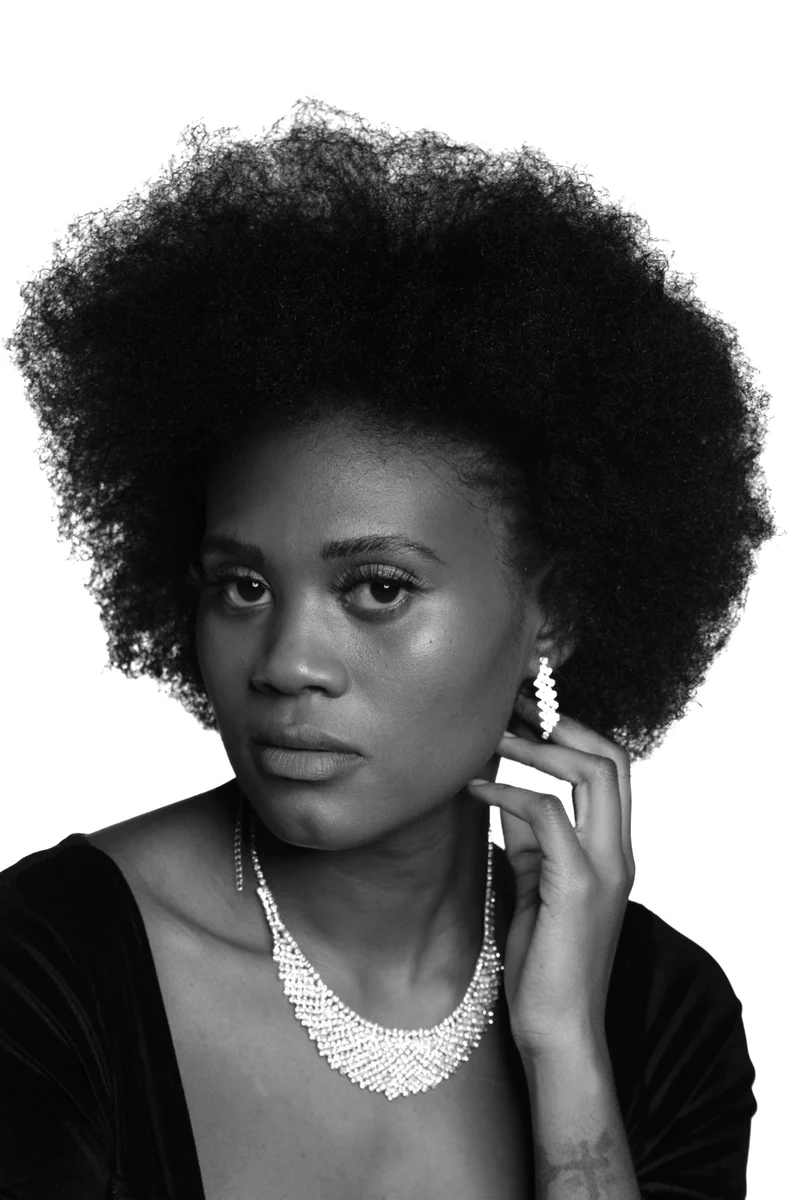 Black-and-white portrait of a woman with an afro and crystal earrings, looking straight at the camera