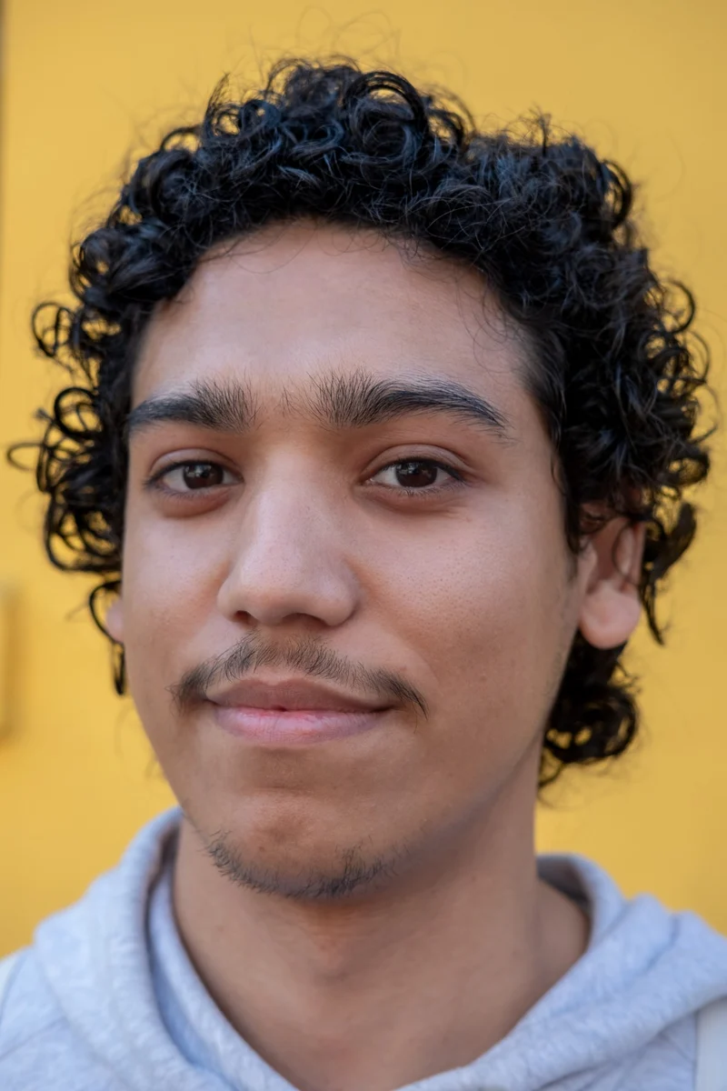 Close-up portrait of a young man with curly hair against a yellow wall