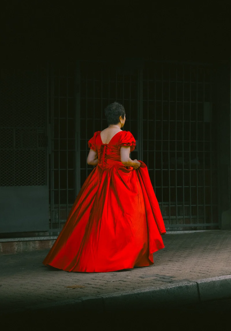 Woman in a red ball gown walking past a barred shopfront