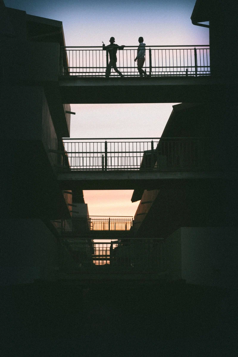 Two figures silhouetted on stacked walkways against a dusk sky