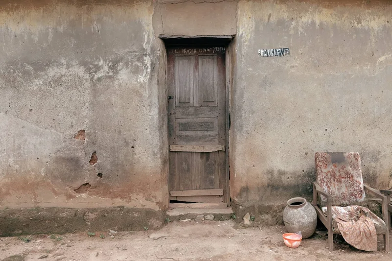 Weathered wooden door in a cracked plaster wall, a clay pot and worn armchair beside it