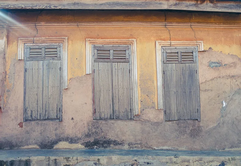 Three grey louvred shutters in a peeling ochre wall