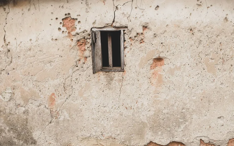 Small window with one shutter open in a pitted, crumbling wall