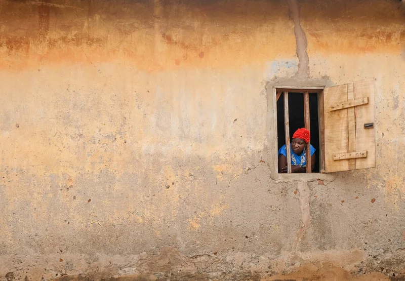 A woman in a red headwrap leaning out of a window in an orange wall