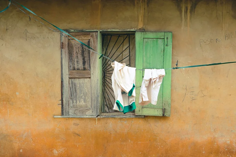 Laundry on a line across a window with one green and one bare wooden shutter