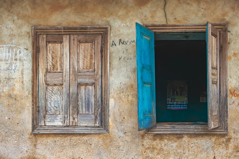 A closed wooden window beside an open one with bright blue shutters