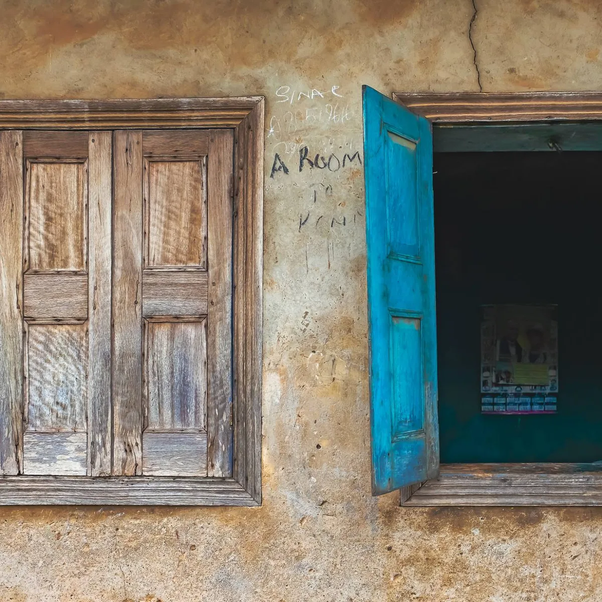 A closed wooden window beside an open one with bright blue shutters
