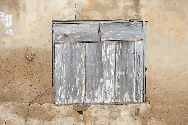 Boarded window of sun-bleached grey planks in a cracked tan wall