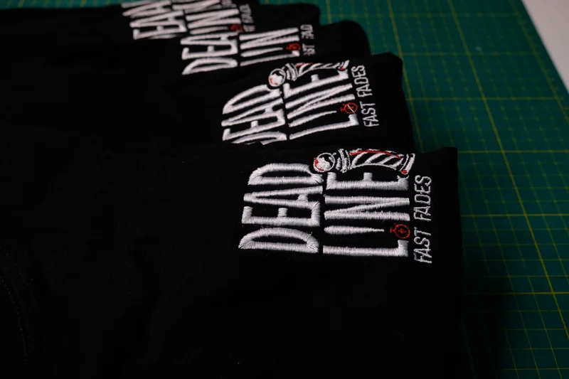 Row of black garments embroidered with the Deadline Fast Fades barbershop logo