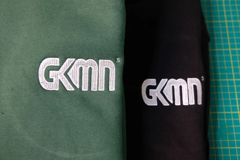 GKMN logo embroidered in white on green and black garments