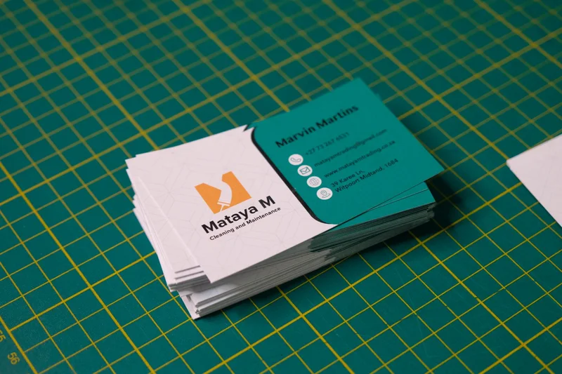 Stack of printed Mataya M Cleaning and Maintenance business cards on a cutting mat