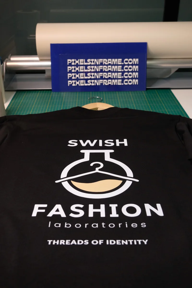 Black T-shirt printed with the Swish Fashion Laboratories logo, on a hanger in the studio